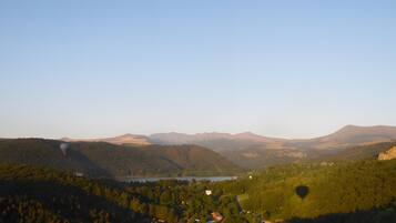 A panoramic view of a valley with a lake, forested hills, and a small settlement.