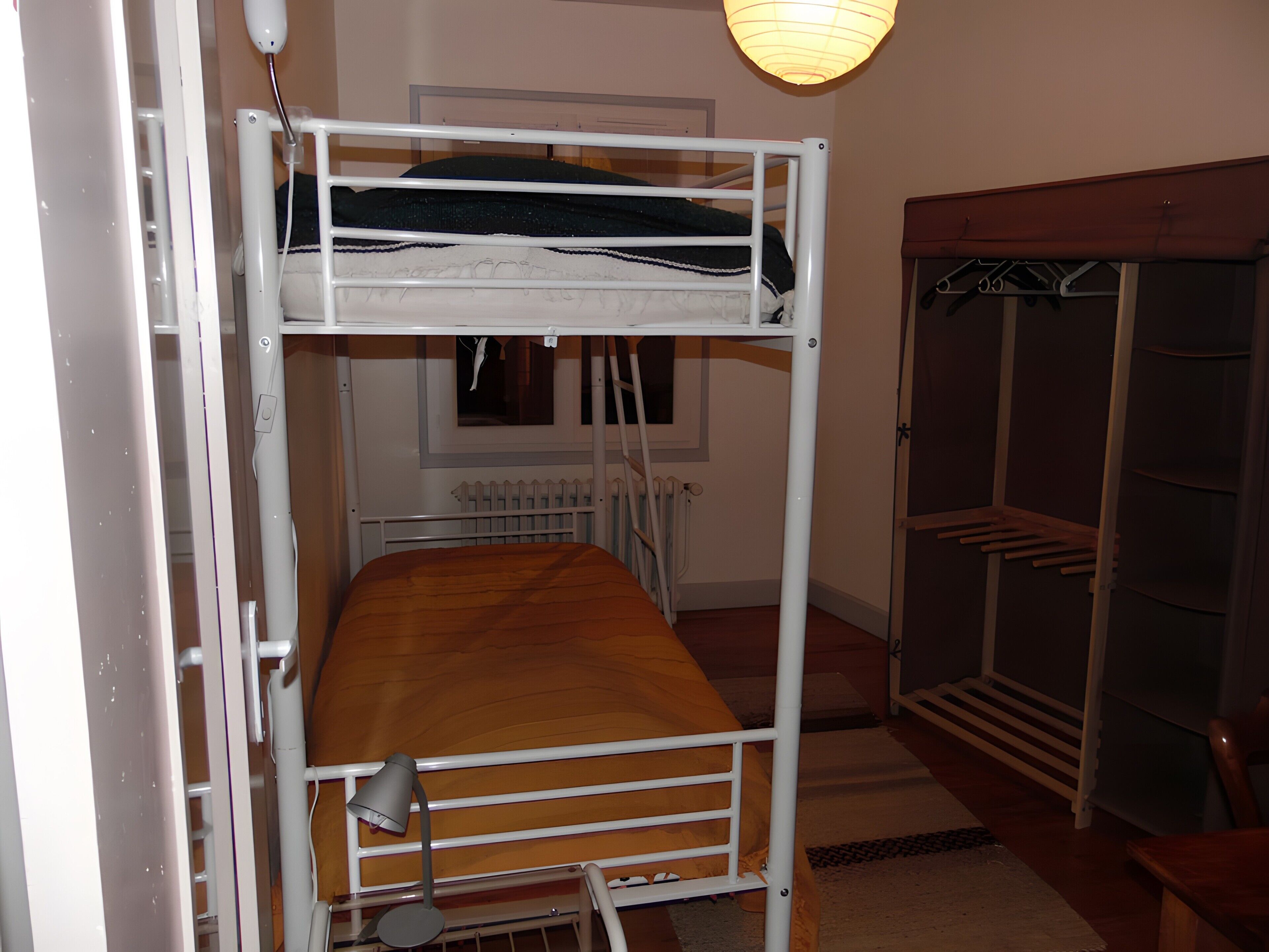 Ein Stockbett mit Schreibtisch und Stuhl, einem Heizkörper und einem Kleiderschrank mit Kleiderstange.