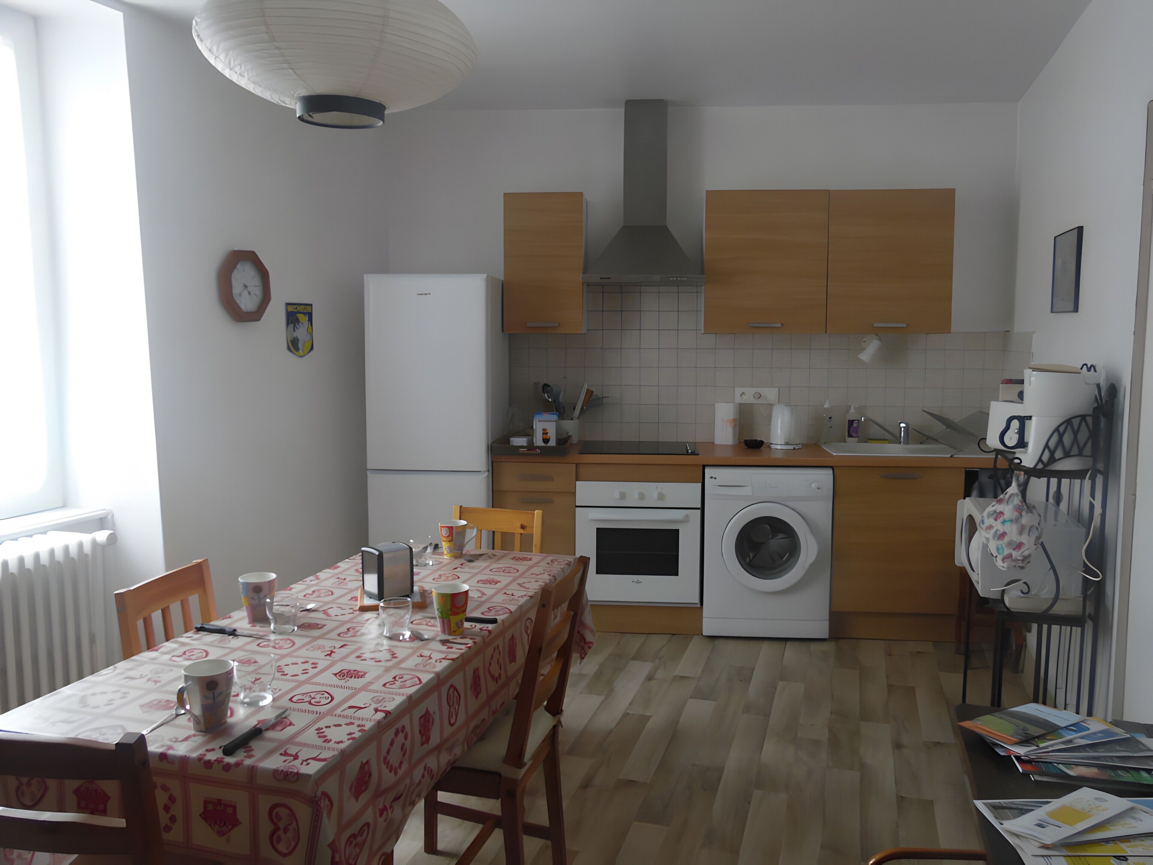 A compact kitchen with a dining area, equipped with a refrigerator, oven, washing machine, and a coffee maker.