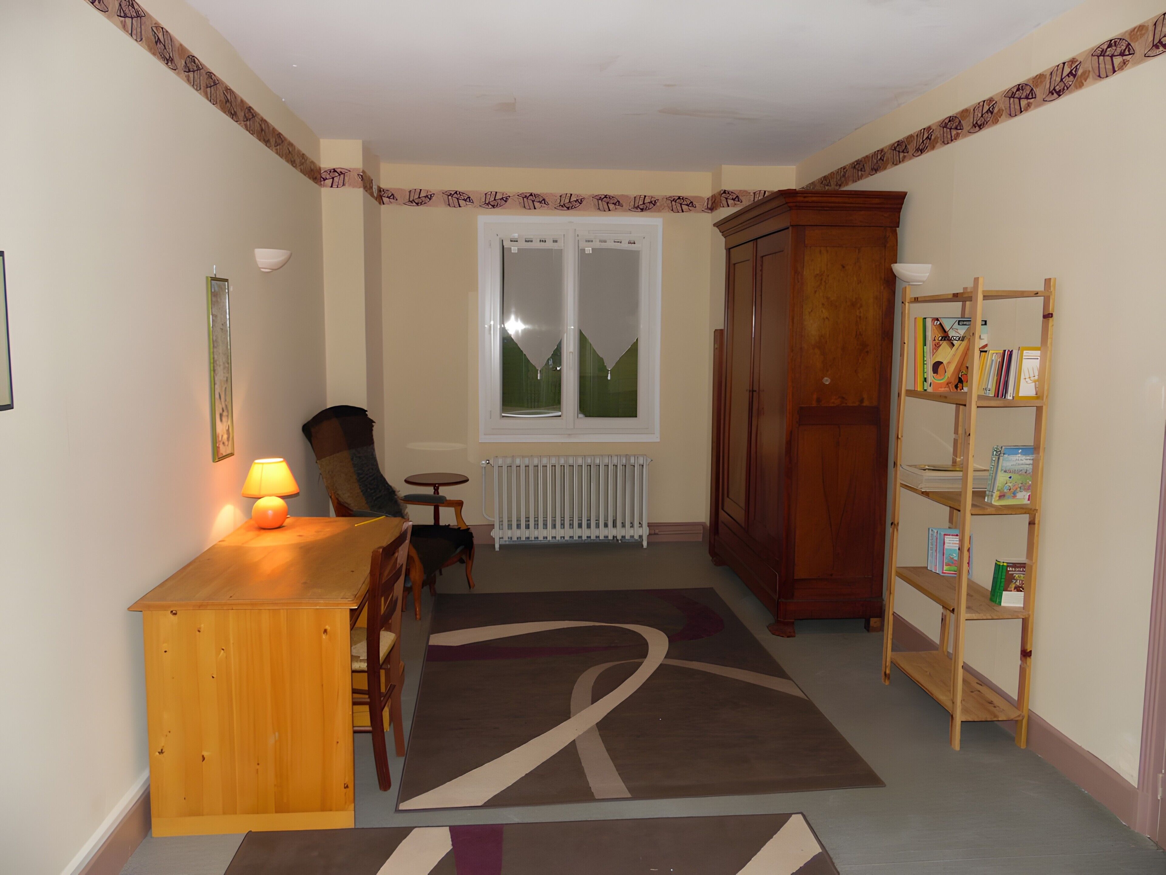 Een kamer met een houten bureau, stoel, radiator, boekenkast en een raam met uitzicht op glooiende groene heuvels.