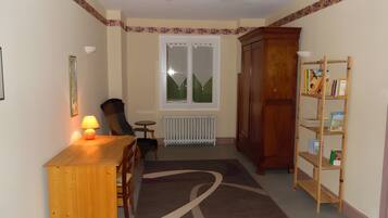 Een kamer met een houten bureau, stoel, radiator, boekenkast en een raam met uitzicht op glooiende groene heuvels.