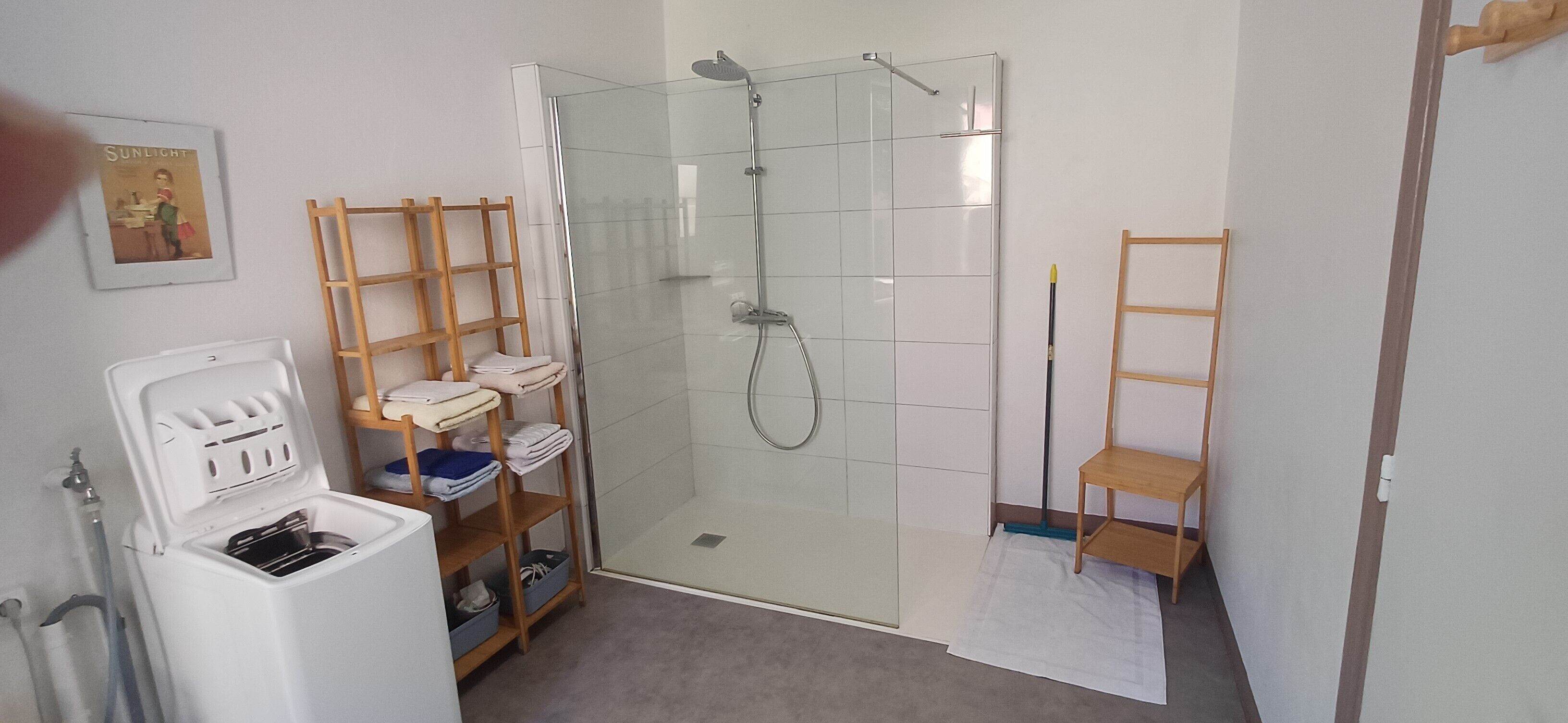 Ein Badezimmer mit einer gläsernen Dusche, einem weißen Waschbecken und einem Holzbodenregal.