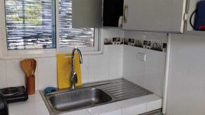 Una cocina con un lavamanos de acero inoxidable, una ventana con persianas y un salpicadero de azulejos.