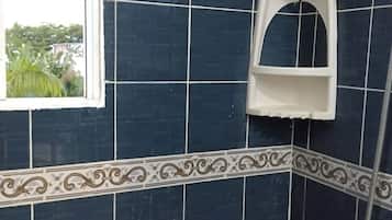 Casa de banho com azulejos azul escuro, chuveiro e janela com vista para vegetação.