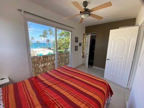 A bedroom with a bed, a ceiling fan, a sliding glass door to a balcony, and a white door. - Kite Beach Hostel (Cabarete)