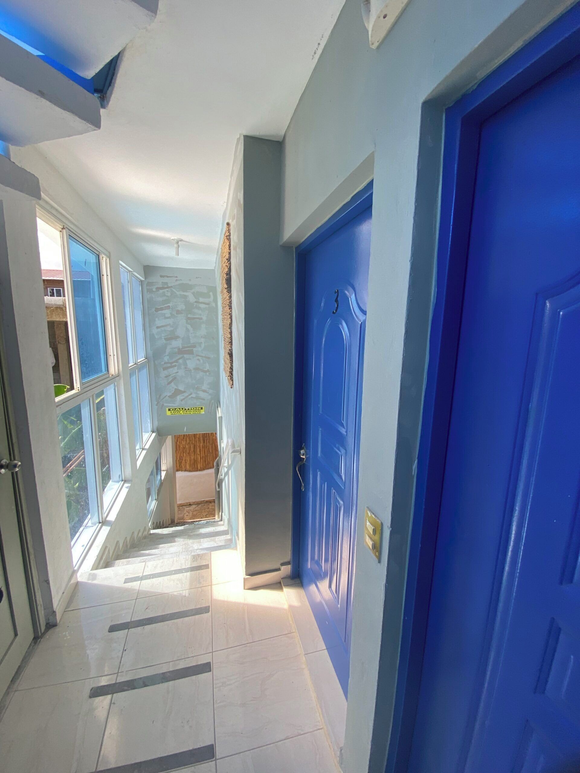 A hallway with a blue door, a staircase, and a view of the outside.