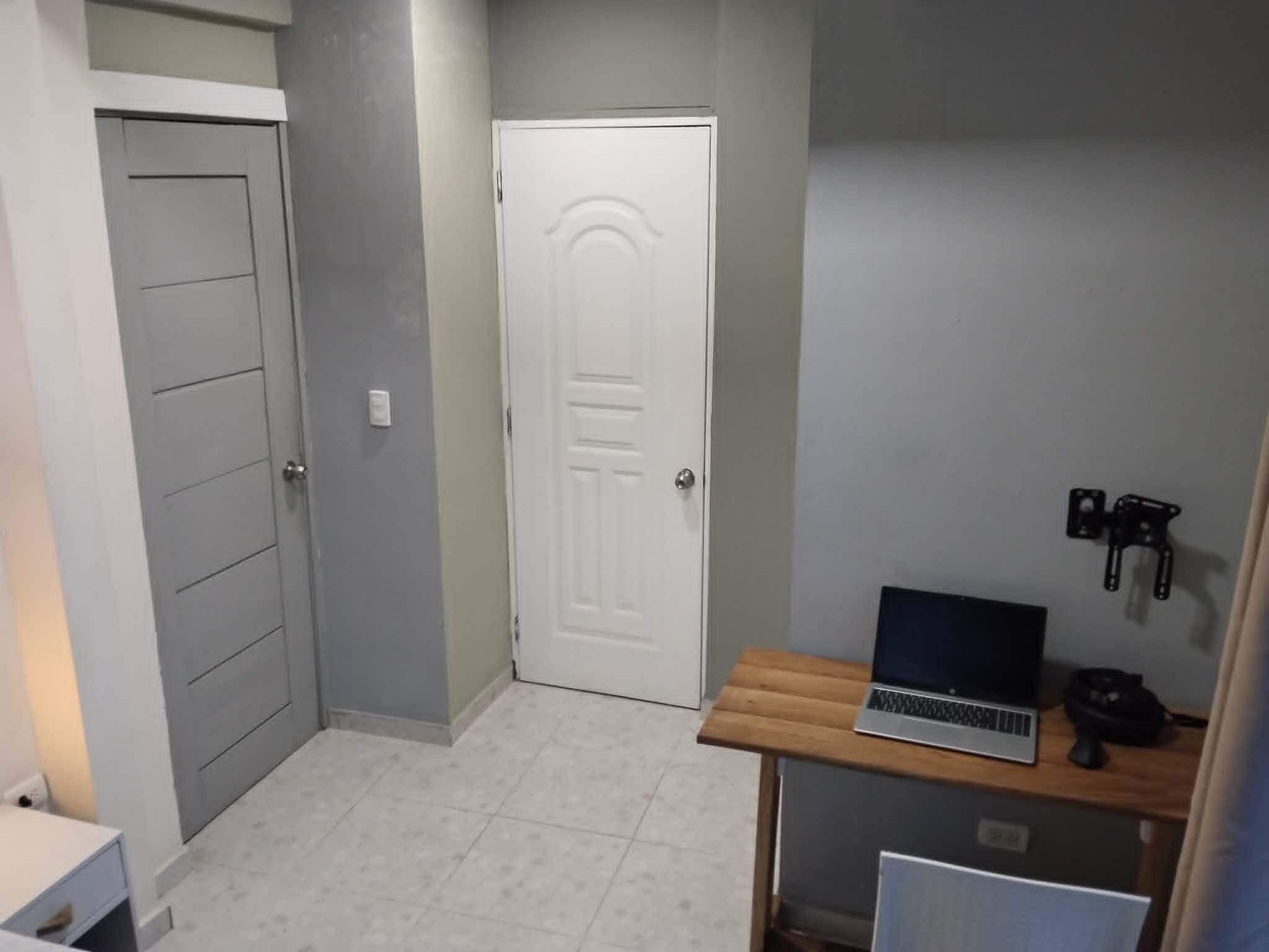 A hallway with a door, a small table with a laptop, and a wall-mounted light fixture.