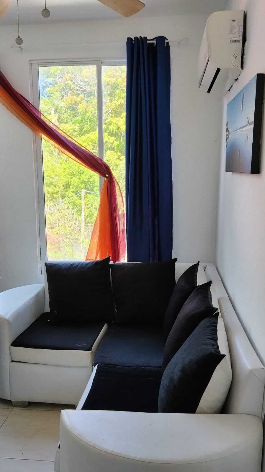 Een kamer met een witte bank, een raam met gordijnen en een plafondventilator.
