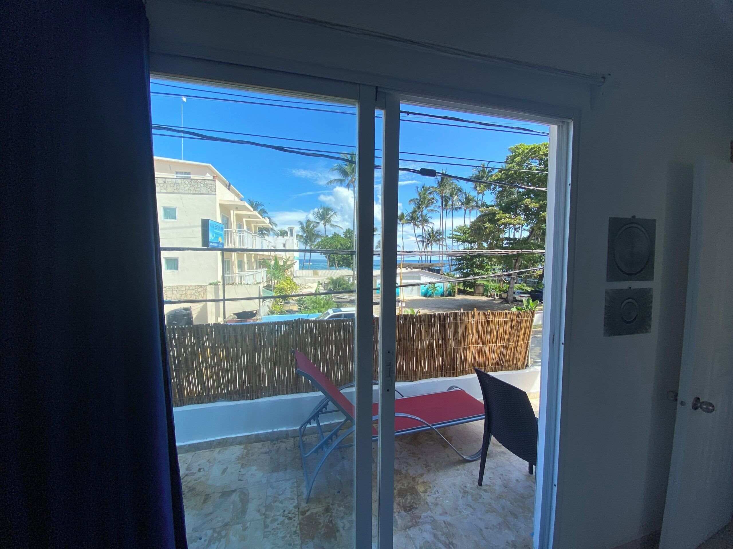 A room with a sliding glass door leading to a balcony with a red chair and a bamboo fence.