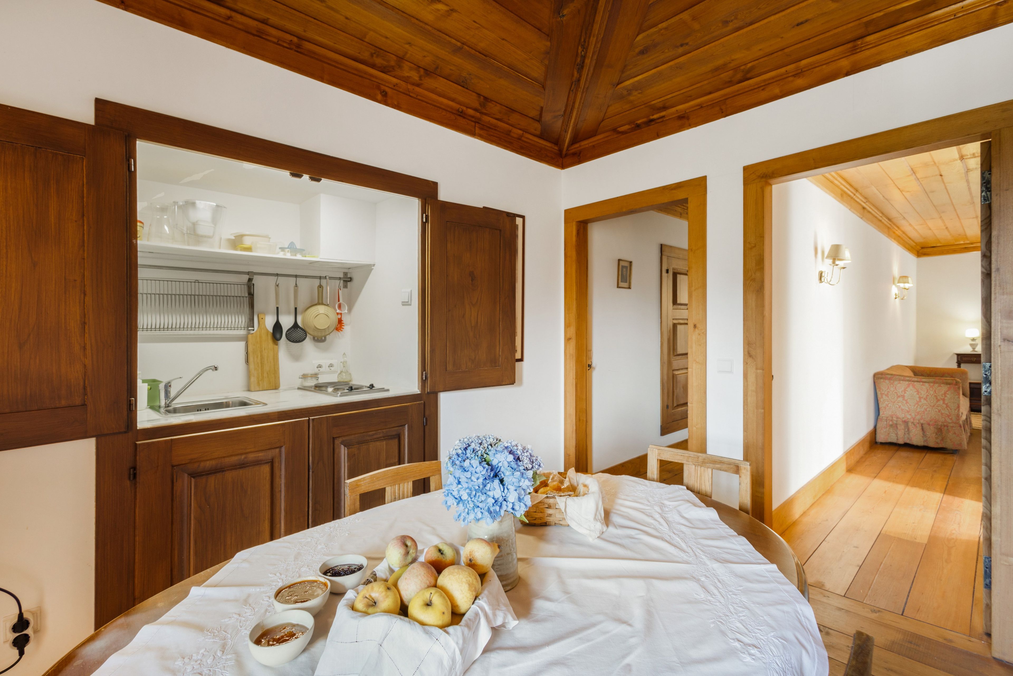 Un'area pranzo con tavolo apparecchiato, una cucina con mobili in legno e un corridoio che porta a un'altra stanza.