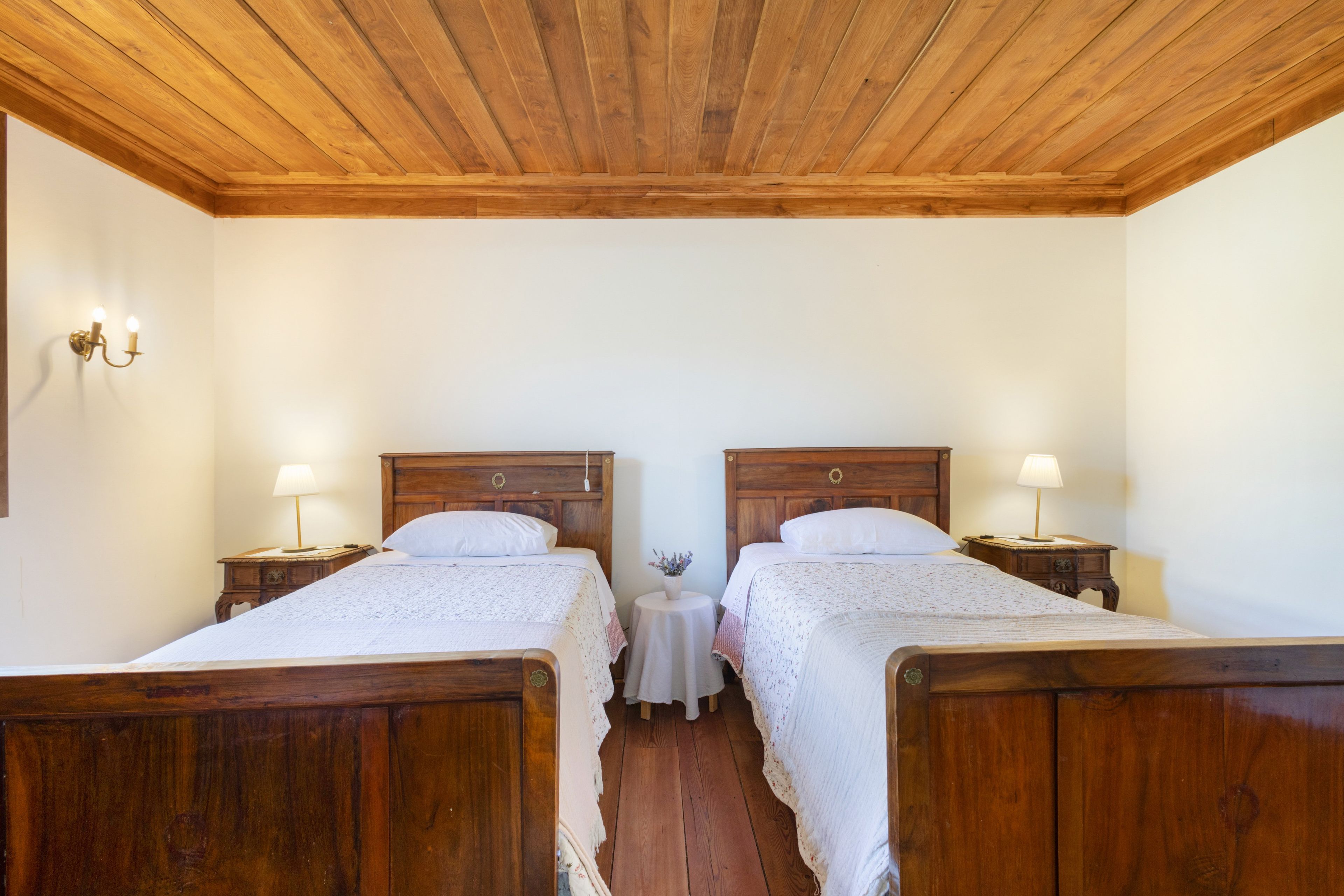 Una stanza con due letti in legno, ognuno dotato di comodino e lampada. Al centro, un tavolino rotondo con una lampada.