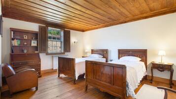 Une pièce avec deux lits en bois, une chaise en bois, une bibliothèque et une fenêtre donnant sur un paysage verdoyant.