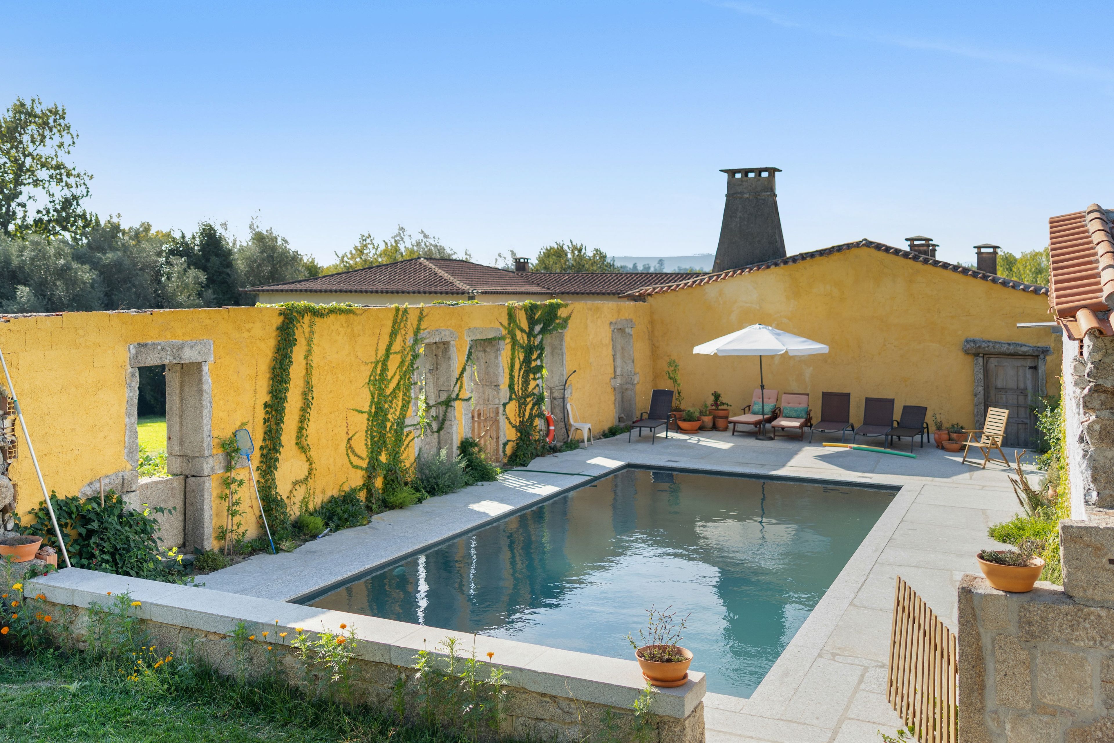 A pool area with a yellow wall, stone pillars, and a tiled roof.