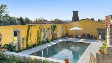 A pool area with a yellow wall, stone pillars, and a tiled roof.