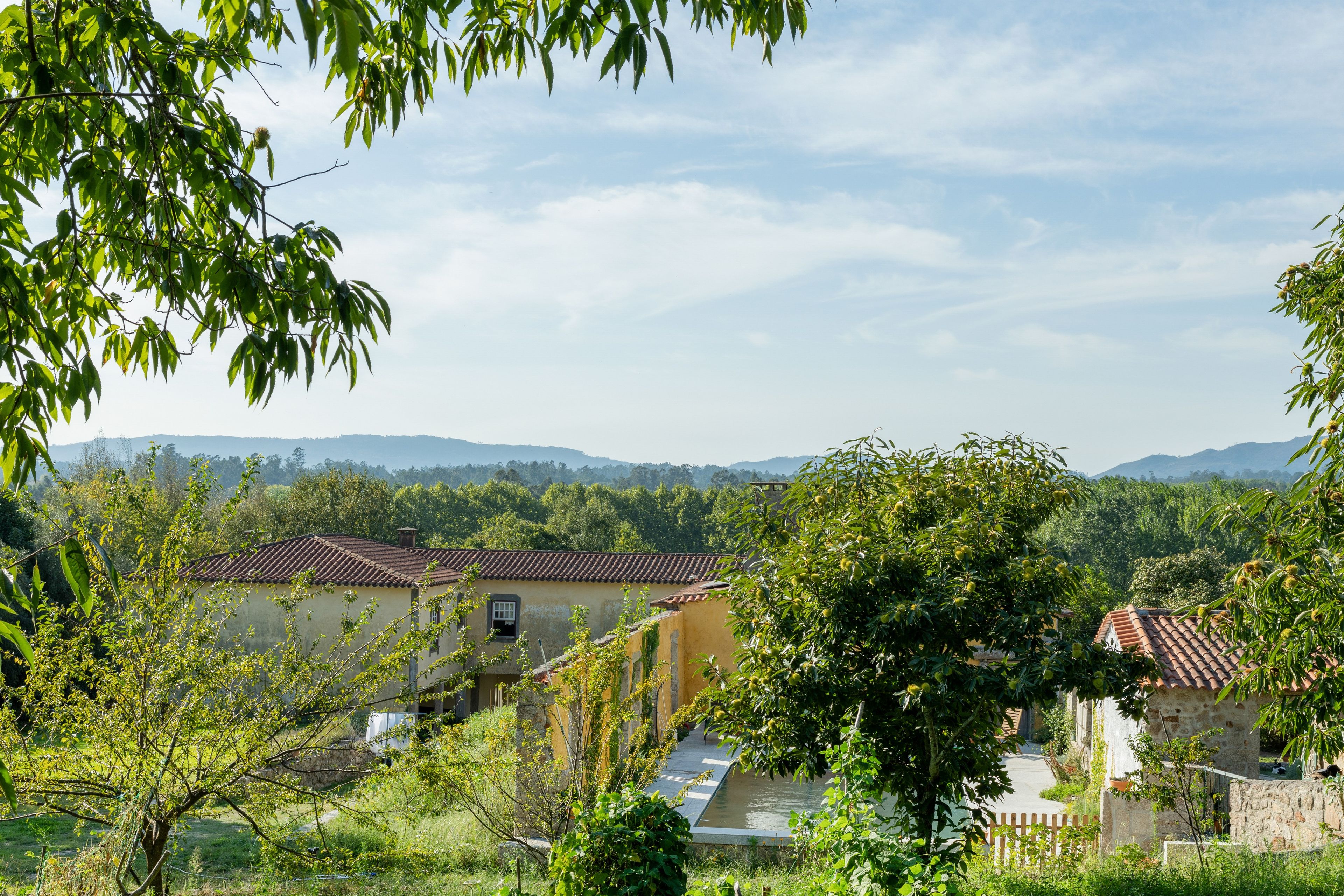 Paesaggio rurale con edifici tradizionali, cielo sereno e catena montuosa in lontananza.