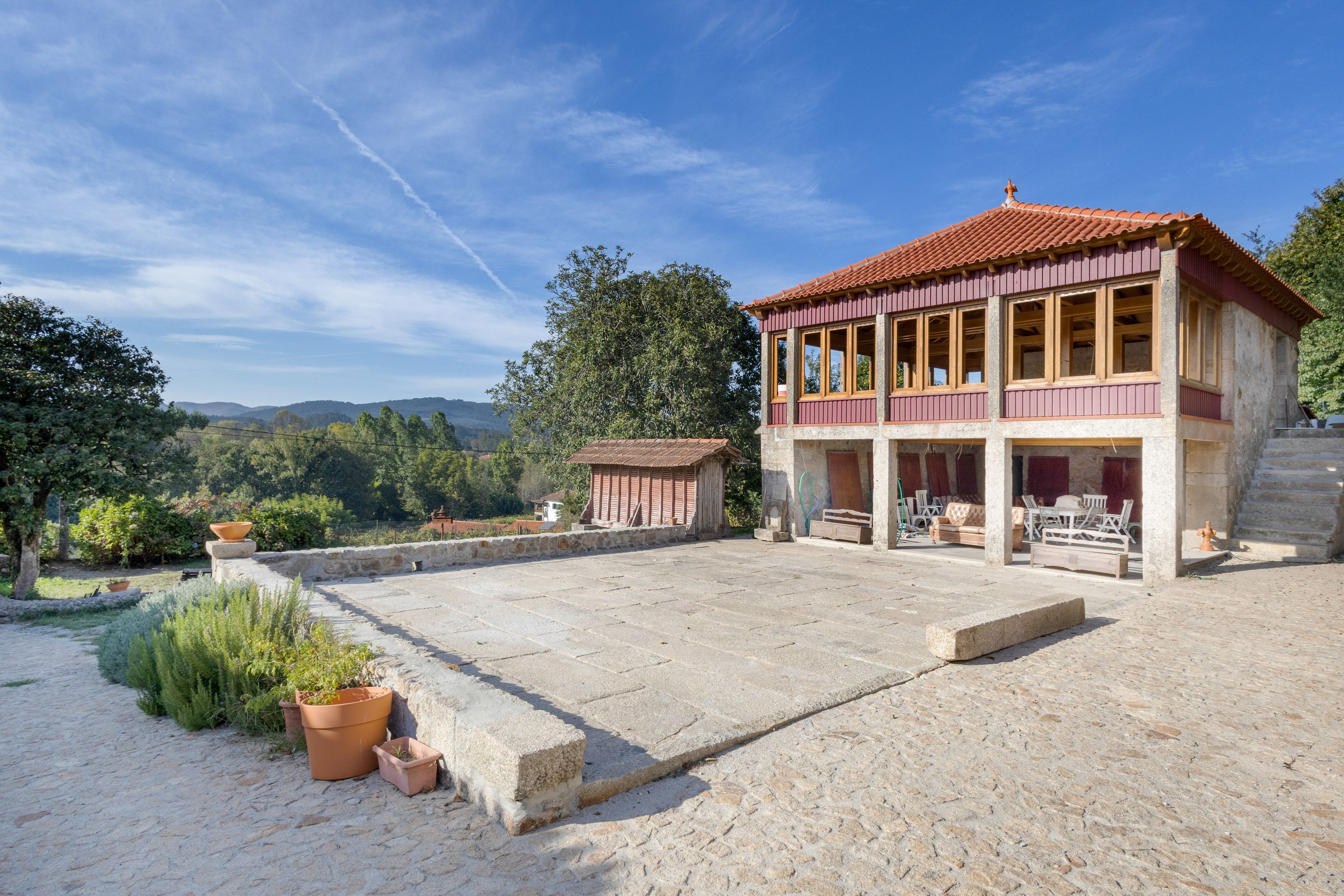 Un bâtiment à deux étages, avec un toit recouvert de tuiles rouges, un balcon doté de balustrades en bois et une cour pavée de pierres.