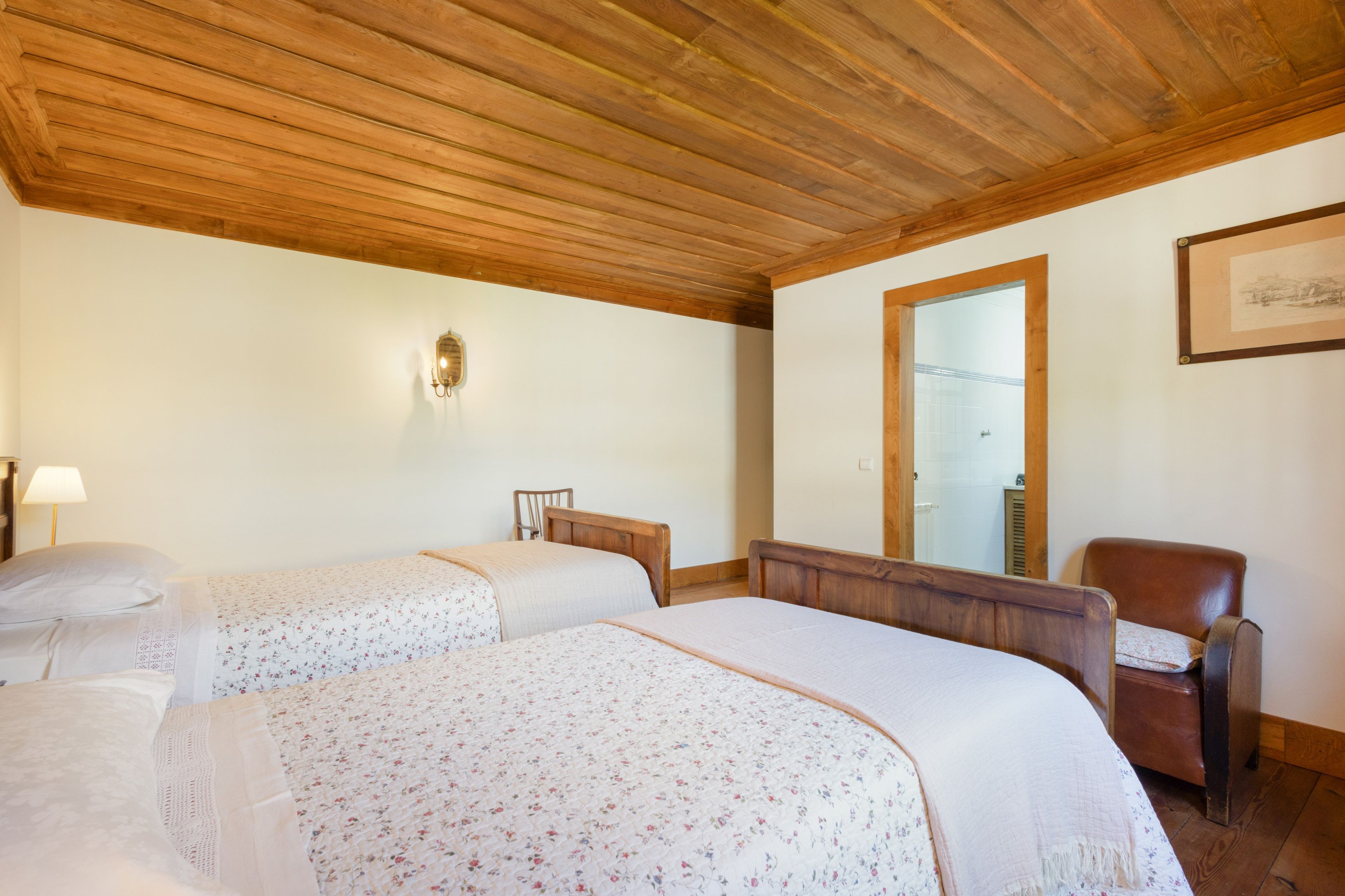 Une chambre avec deux lits, un plafond en bois, un miroir et un tableau encadré au mur.