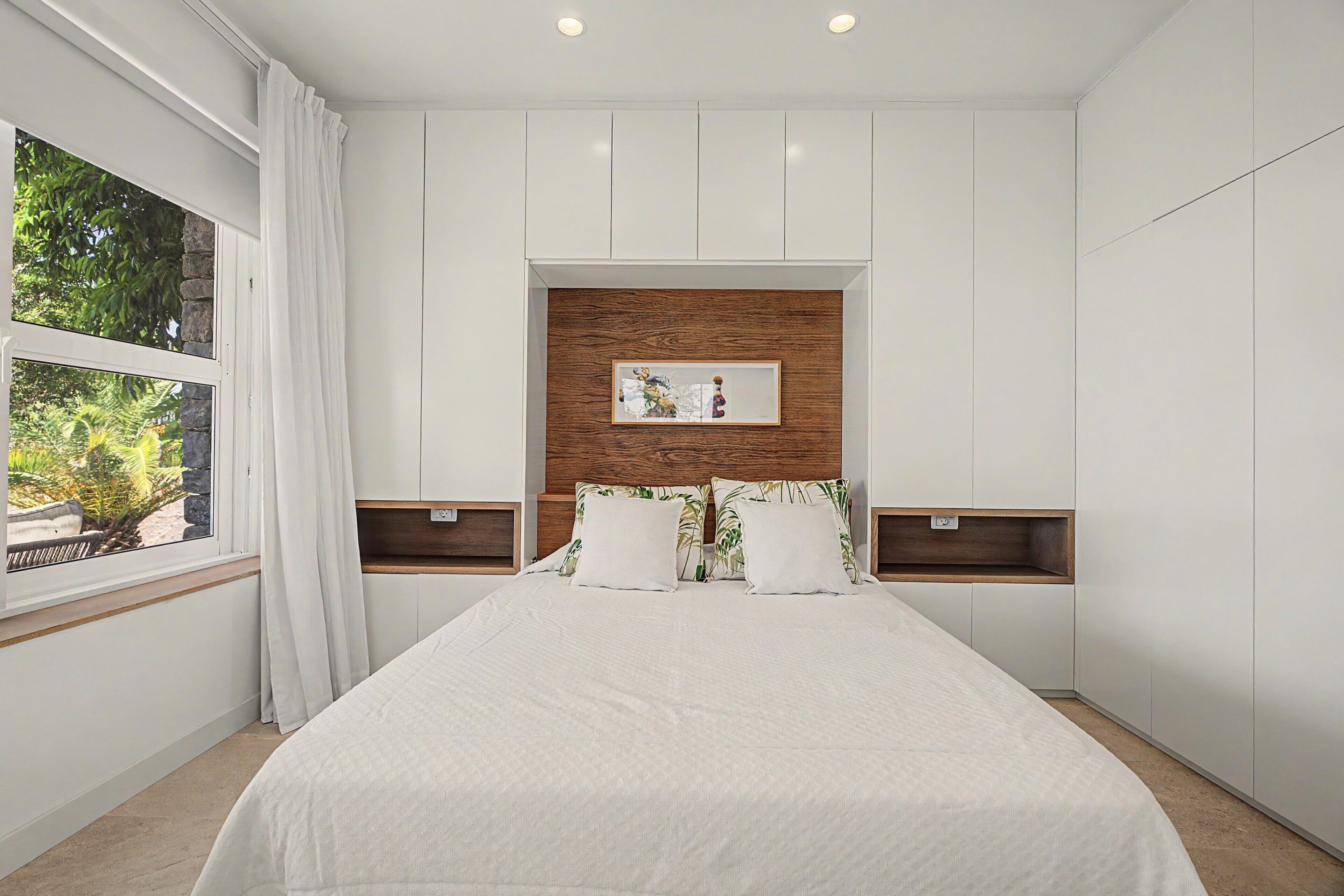 A bedroom with a bed, a window with curtains, a wooden headboard, and bedside tables.