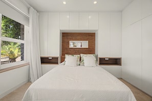 Un dormitorio con cama, ventana con cortinas, cabecera de madera y mesitas de noche.