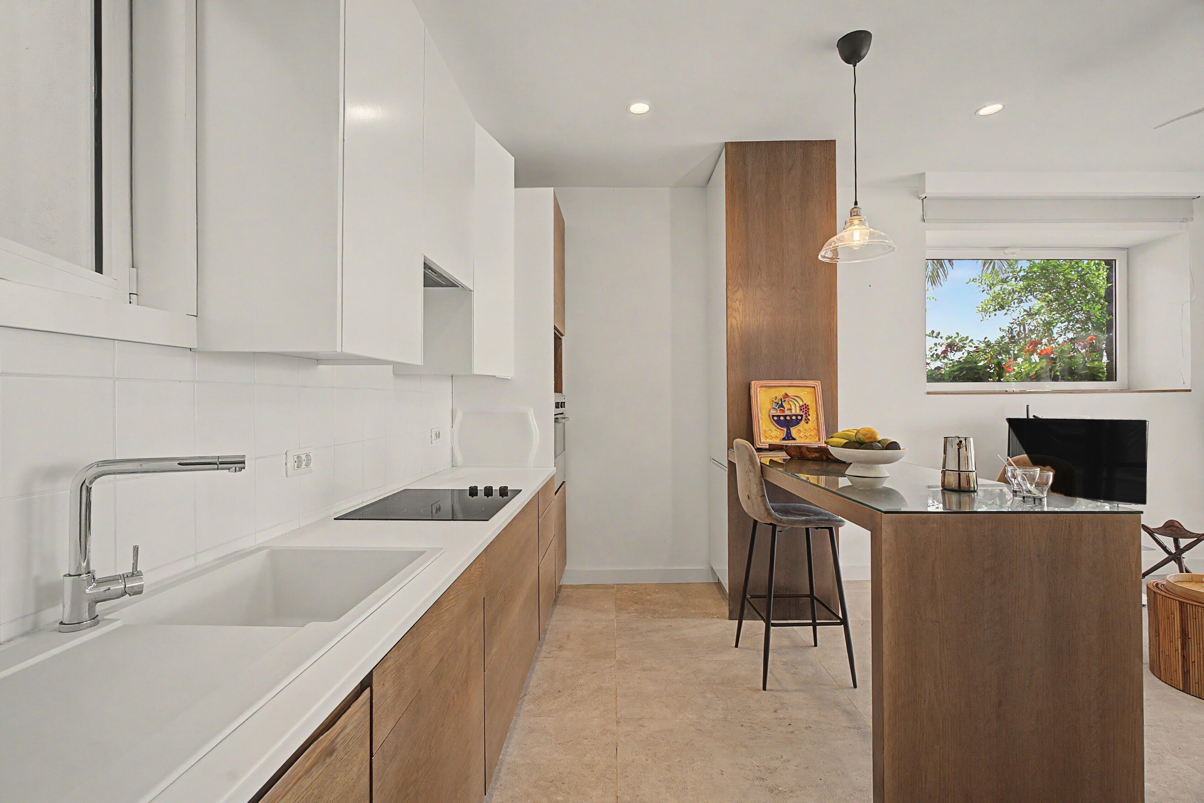 Una cocina moderna con armarios blancos, una isla de madera y un comedor con vistas a zonas verdes.