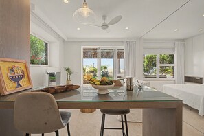 Una habitación de hotel moderna con una mesa de comedor de vidrio, un ventilador de techo y vistas al exterior.