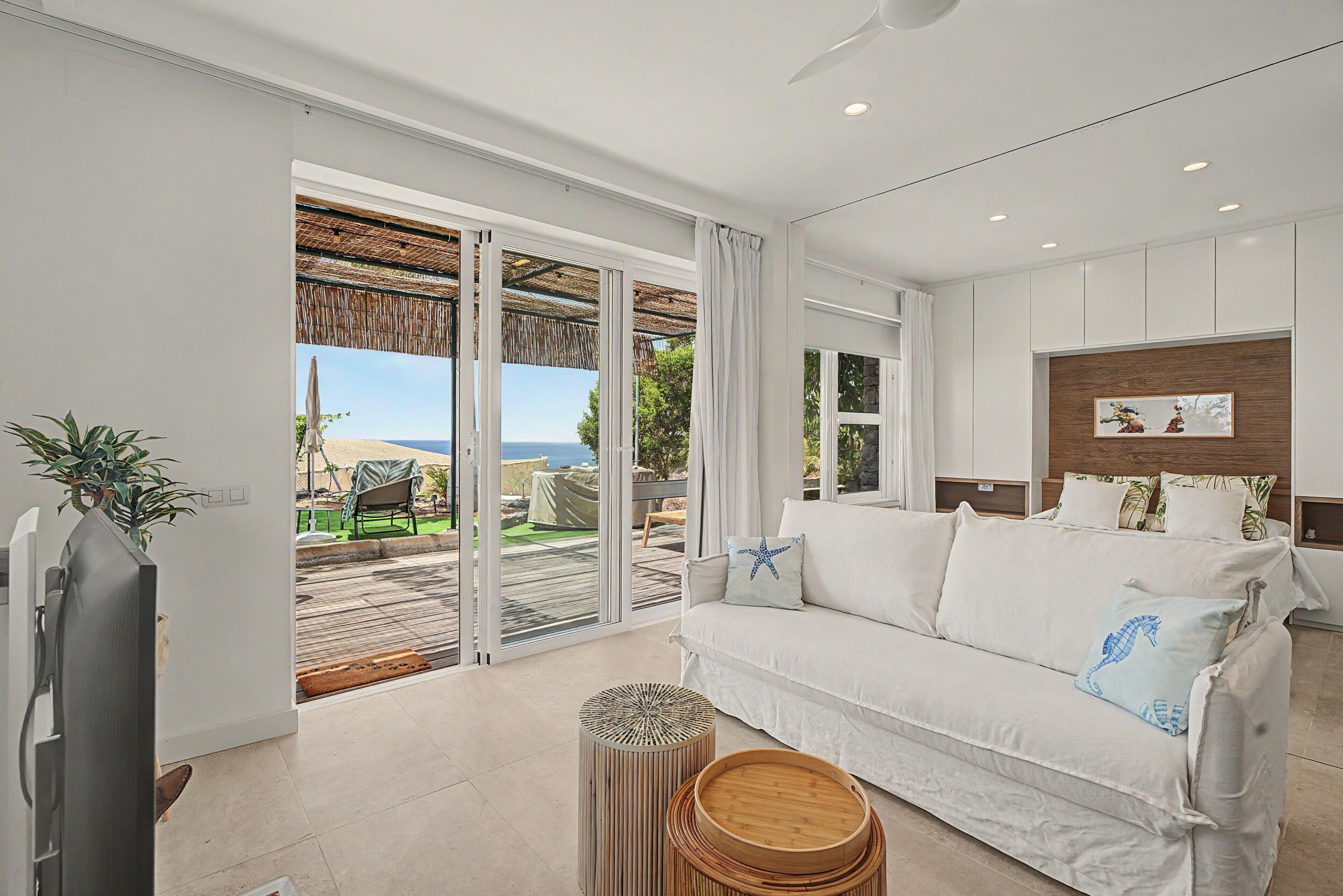 A modern living room with a white sofa, a television, and a view of the outdoors.
