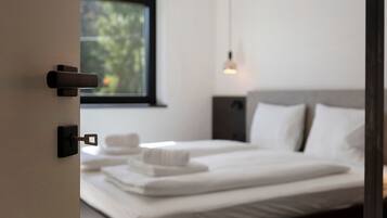 Ein Hotelzimmer mit Bett, Fenster, einer Pendelleuchte und einer Tür mit Schlüsselloch.
