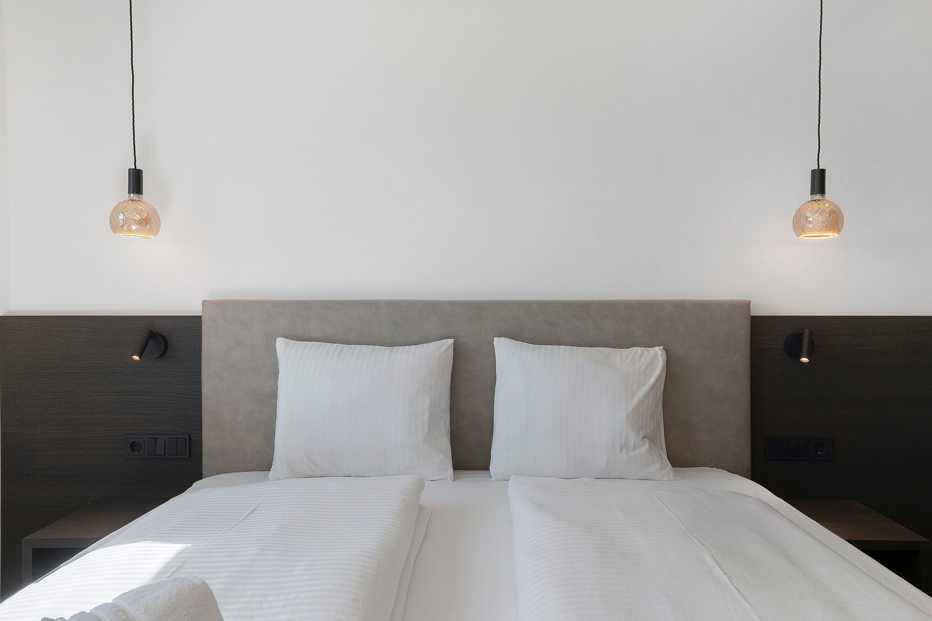 A double bed with white bedding, two bedside tables, and two wall-mounted lamps.