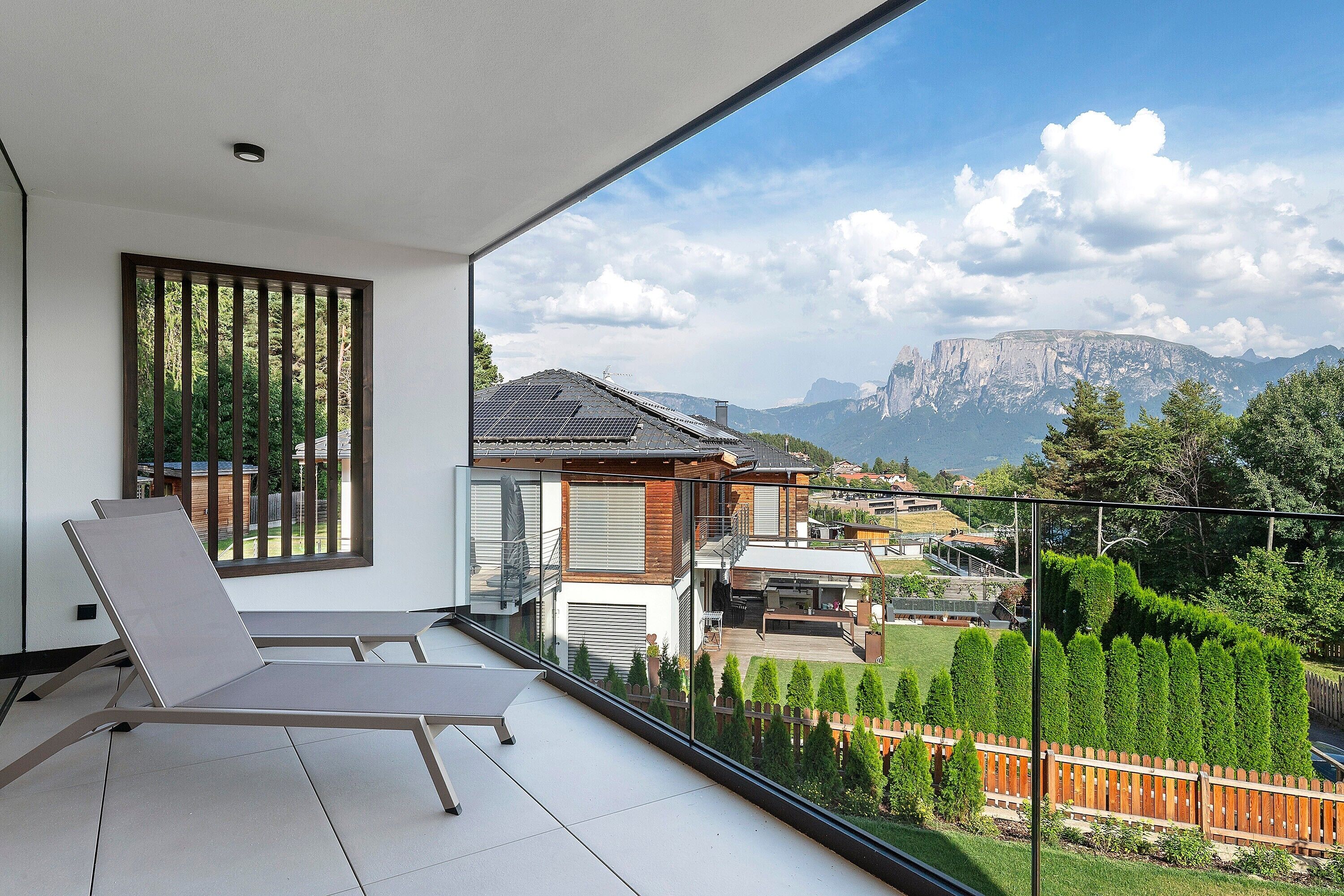 Un balcón con vista a una cadena montañosa, una silla y un edificio con paneles solares.