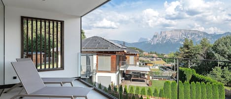 Un balcón con vista a una cadena montañosa, una silla y un edificio con paneles solares.