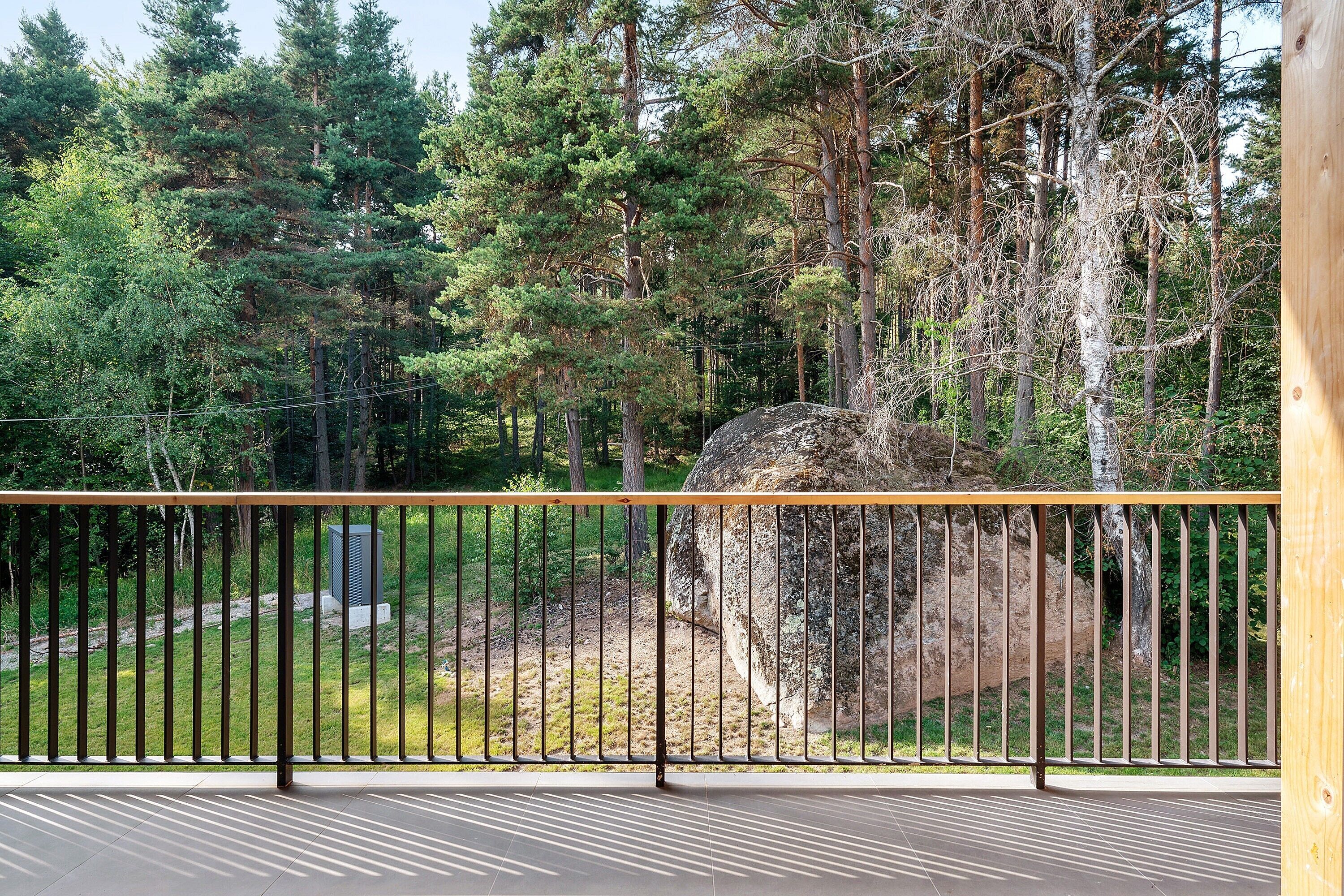 A balcony with a metal railing overlooking a forested area with a large rock and trees.