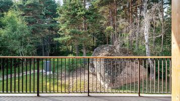 A balcony with a metal railing overlooking a forested area with a large rock and trees.