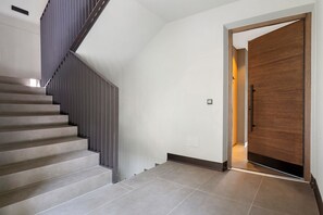 Eine modern gestaltete Treppe führt zu einem Raum mit einer Holztür und einem Lichtschalter an der Wand.