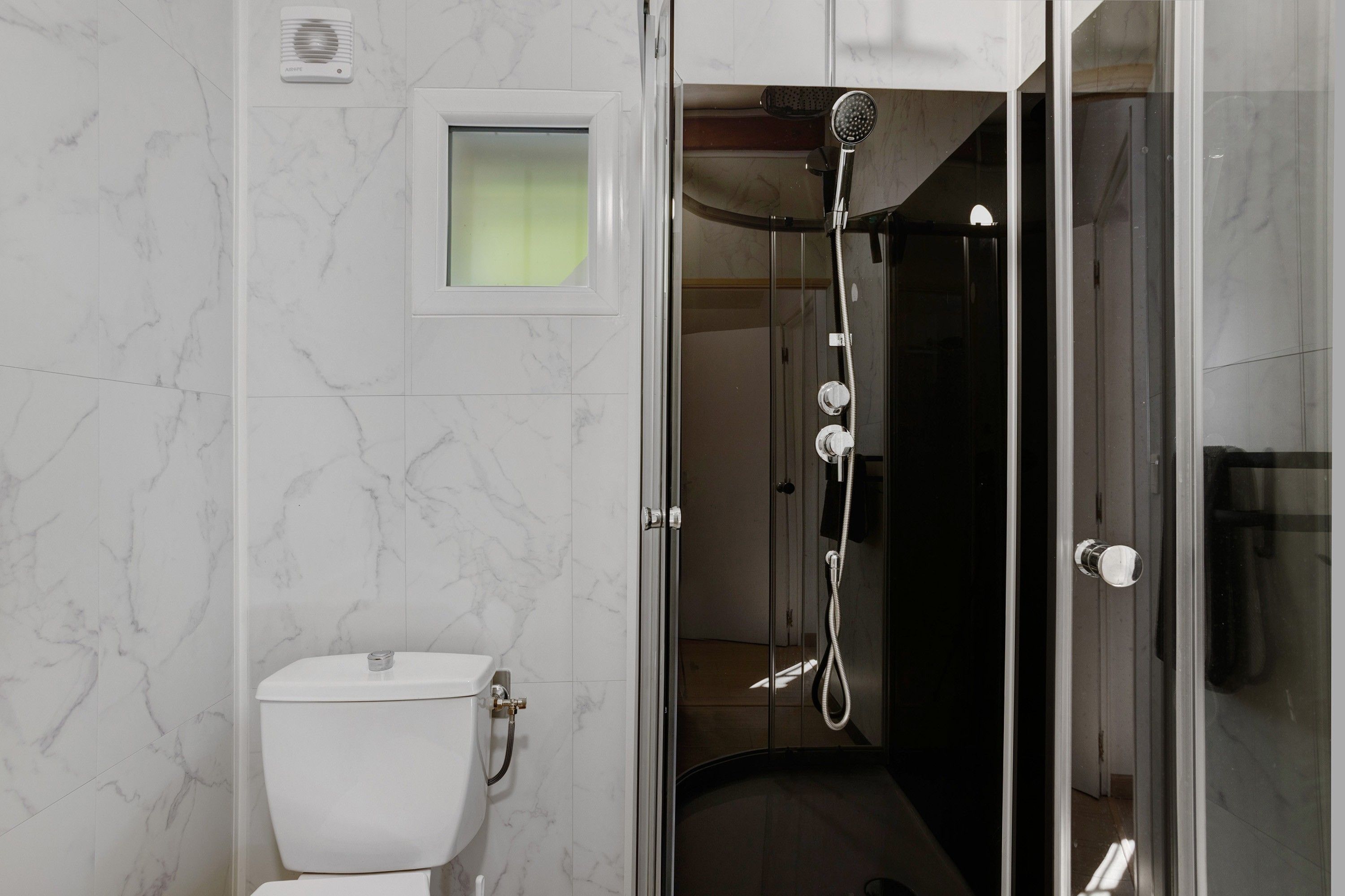 Un baño moderno con inodoro, cabina de ducha y puerta de vidrio.