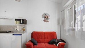 A compact living space with a kitchenette, a red sofa with cushions, and a decorative wall piece.