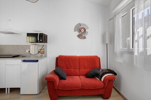A compact living space with a kitchenette, a red sofa with cushions, and a decorative wall piece.