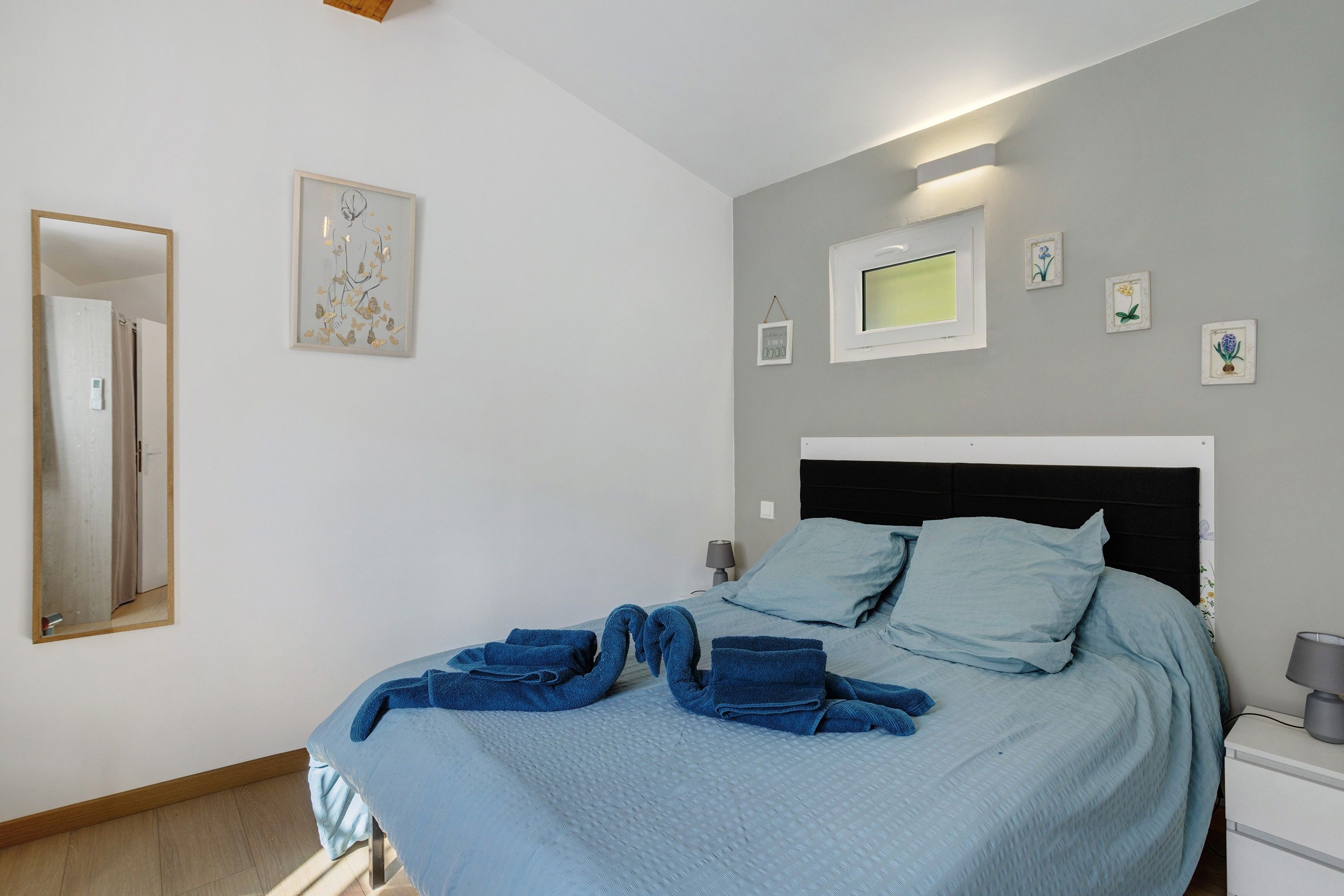 Een slaapkamer met een bed, nachtkastje, lamp en foto's aan de muur.