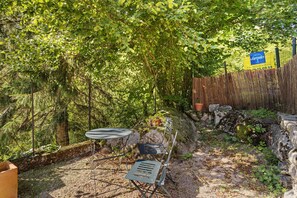 A garden area with a table and chairs, surrounded by dense foliage and a wooden fence.
