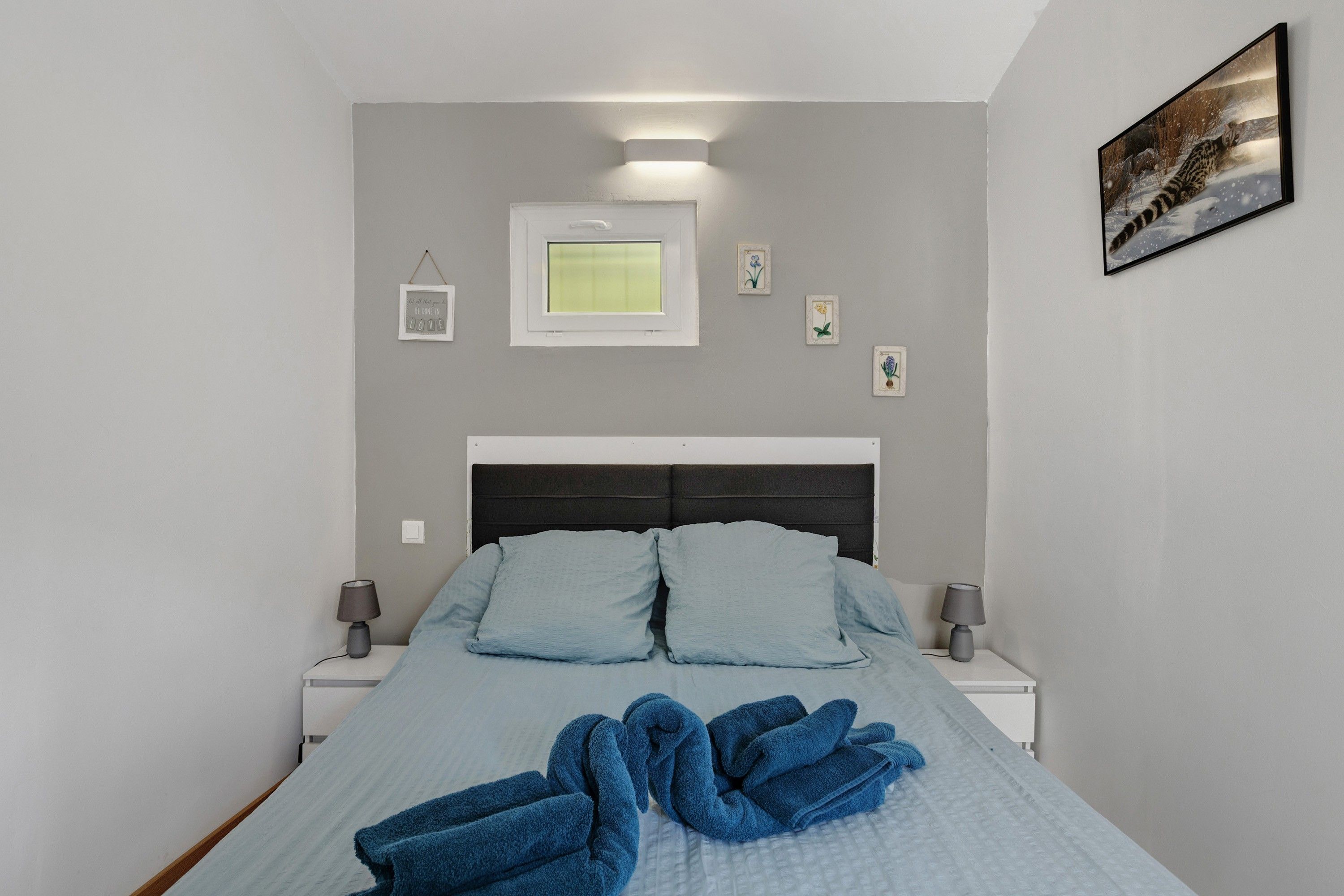 Un dormitorio con cama, dos mesitas de noche, una mesilla auxiliar, un cuadro en la pared y una ventana.