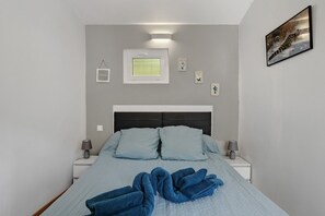 A bedroom with a bed, two bedside tables, a nightstand, a wall-mounted picture, and a window.
