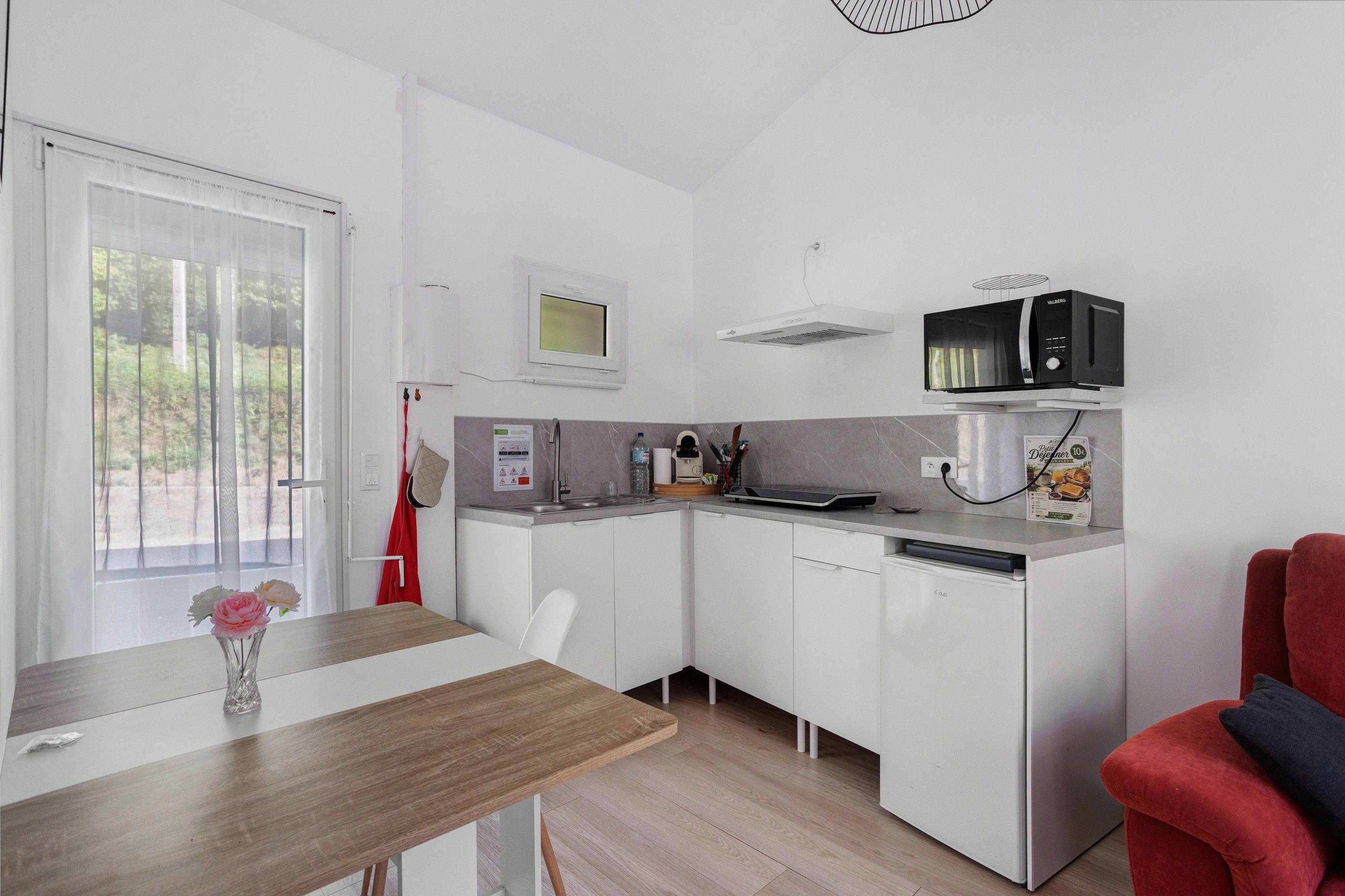 Una cocina compacta con microondas integrado, un lavamanos pequeño y una zona de comedor con mesa y sillas.