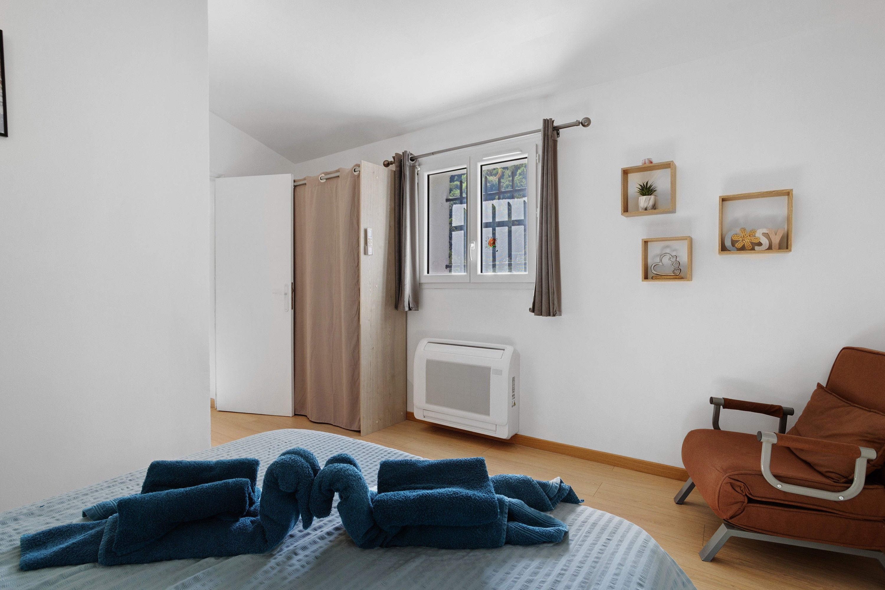 Une chambre à coucher comprenant un lit, une chaise, une fenêtre avec des rideaux, un radiateur et des éléments de décoration murale.