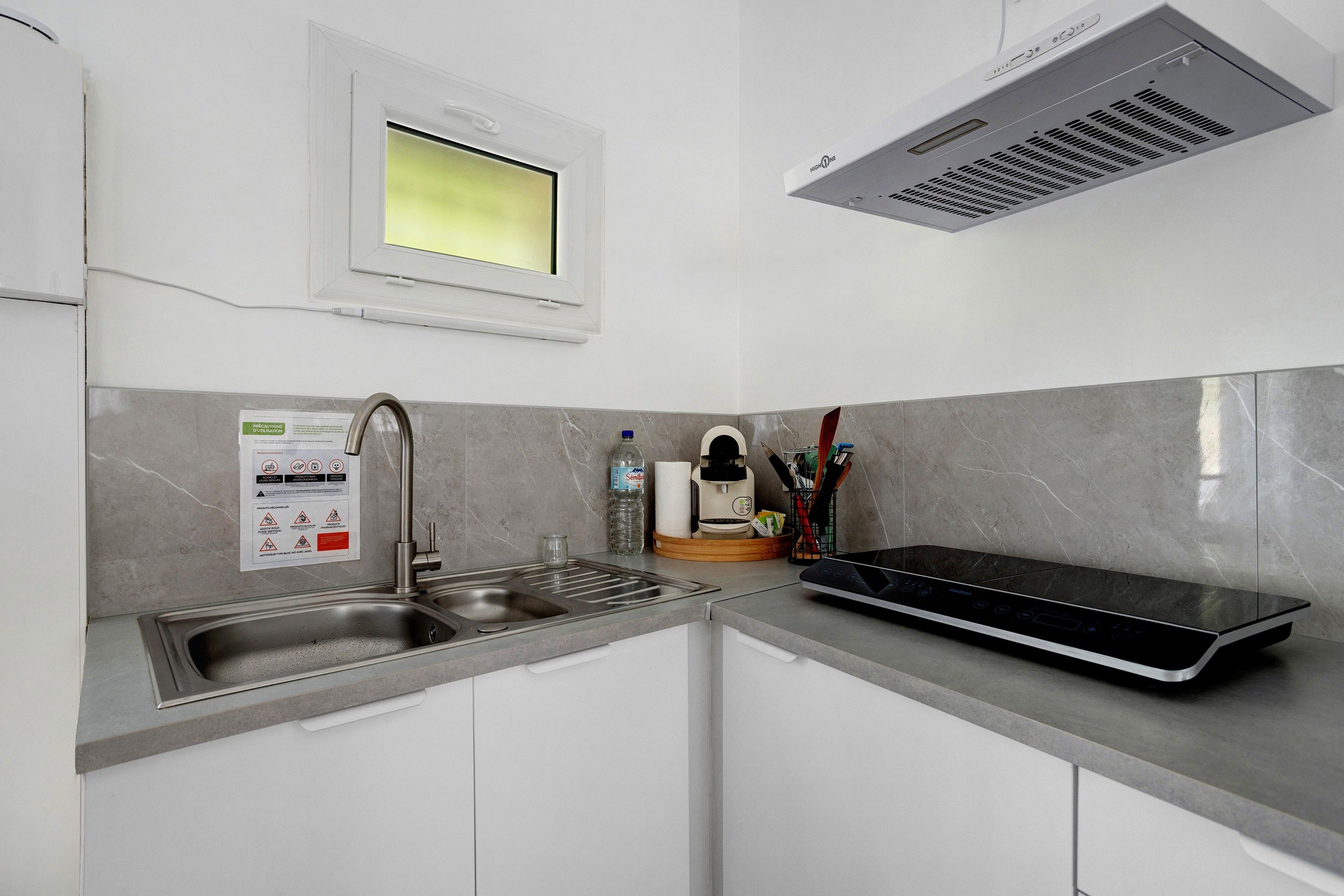 Een moderne keuken met een ingebouwde magnetron, een roestvrijstalen spoelbak en een raam boven de spoelbak.