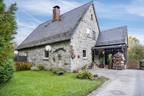 A stone house with a sloped roof, a chimney, and a small porch with potted plants.
