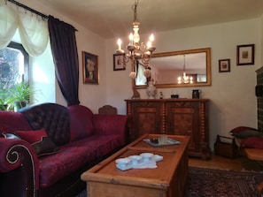 A living room with a red sofa, a wooden coffee table, a chandelier, a mirror, and framed pictures on the wall. - Holiday Home Madlholz with Private Terrace and Garden (Geiersthal)