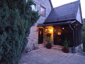 A stone building with a dark roof, a wooden door, and a small porch area with potted plants. - Holiday Home Madlholz with Private Terrace and Garden (Geiersthal)