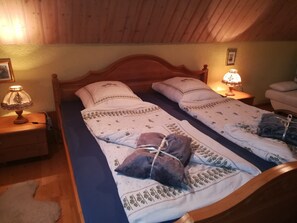 A room with two beds, each with a patterned bedspread and pillows, a wooden headboard, bedside lamps, and a wooden floor. - Holiday Home Madlholz with Private Terrace and Garden (Geiersthal)