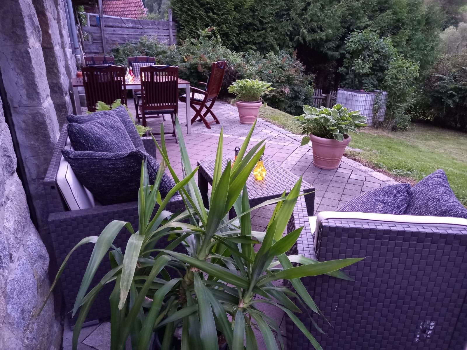 Un patio al aire libre con mobiliario de mimbre, plantas en macetas y un muro de piedra.