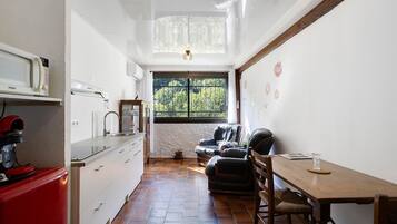 Een smalle keuken met een raam, een eethoek met een tafel en stoelen, en een rode apparatuur aan de linkerkant.