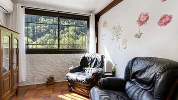 A room with a large window, a leather armchair, a wooden cabinet, and a floral wall decoration.